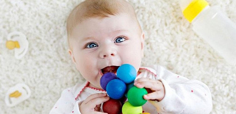 Kleines Baby mit blauen Augen hält Spielzeug in der Hand