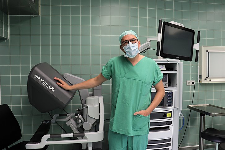 Arzt in grüner OP-Kleidung legt Hand auf den OP-Roboter.