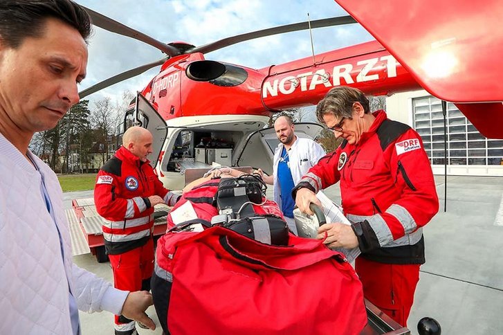 Vier Notfallmediziner kümmern sich um einen Patienten auf einer Trage, die neben einem Rettungshubschrauber steht
