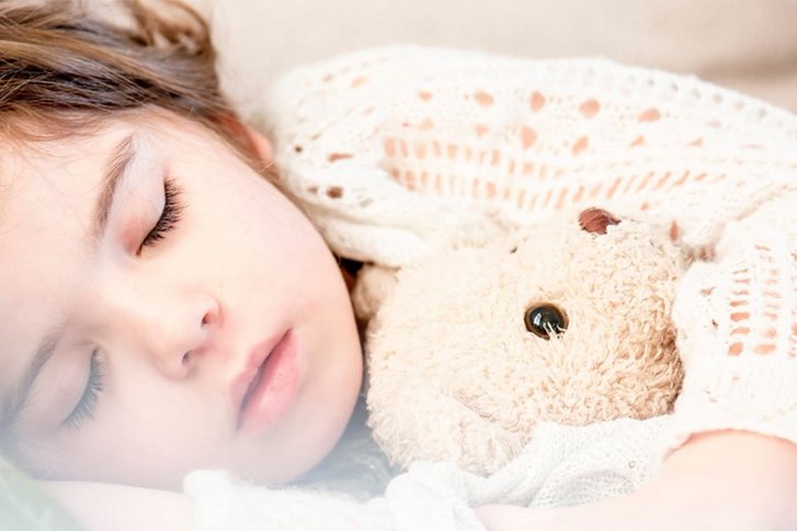 Kleines Mädchen schläft mit Stoffbär im Arm