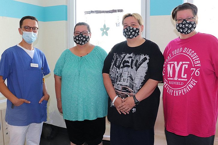 Mann in Arztkleidung und drei Frauen mit Mund-Nasen-Schutz