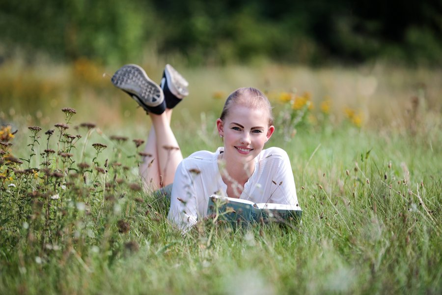 Junge Frau mit Buch liegt im Gras