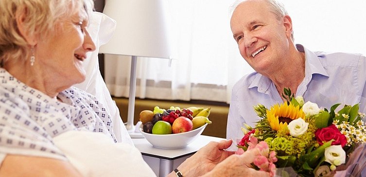 Älterer Mann bringt kranker Frau Blumen ans Krankenbett