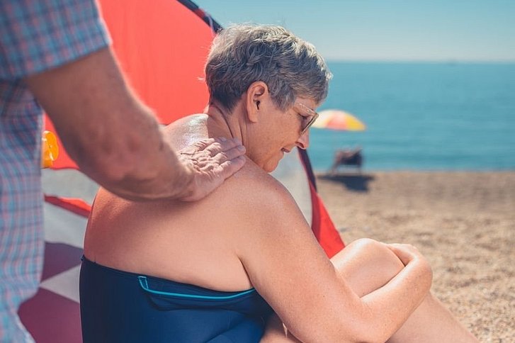 Ältere Dame bekommt Rücken mit Sonnenmilch eingecremt