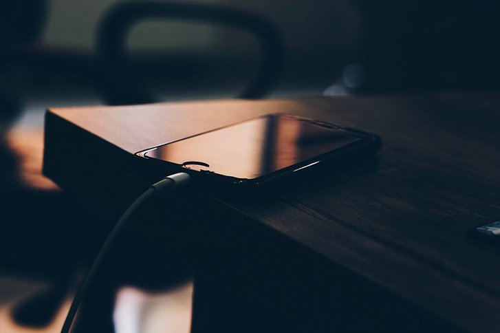 Schwarzes Smartphone liegt auf braunem Holztisch mit Ladekabel