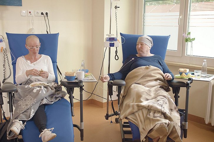 Zwei Frauen sitzen auf Krankenhausstühlen und sind an Infusionsgeräte angeschlossen