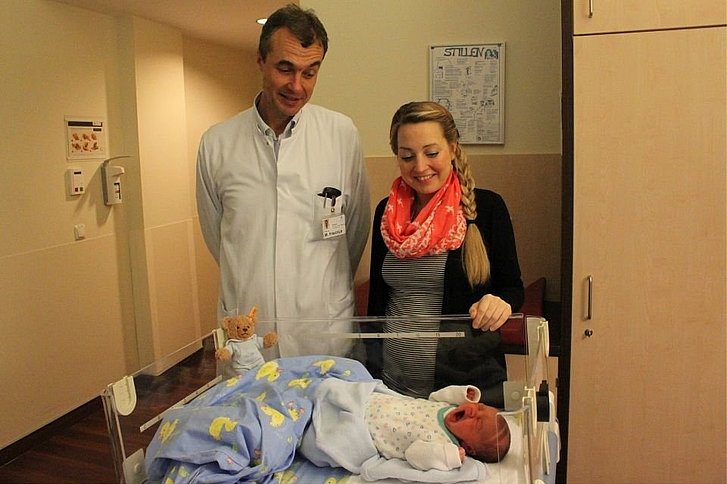 Mann in Arztkittel und Frau blilcken in Kinderbett