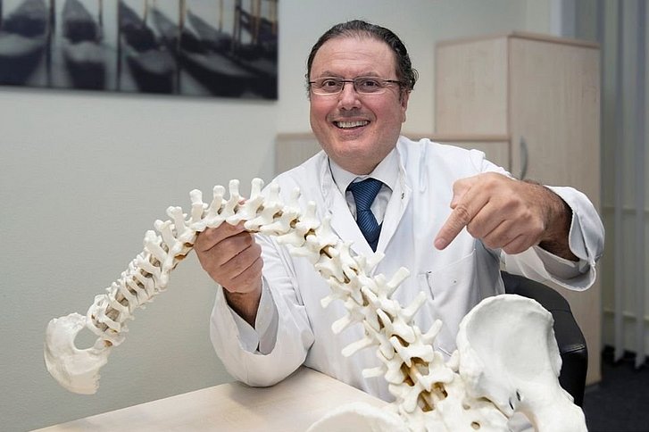 Mann mit Brille im Arztkittel hält abbildung einer Wirbelsäule