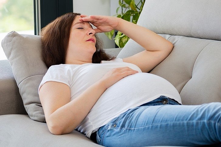 Schwangere mit Kopfschmerzen auf Sofa