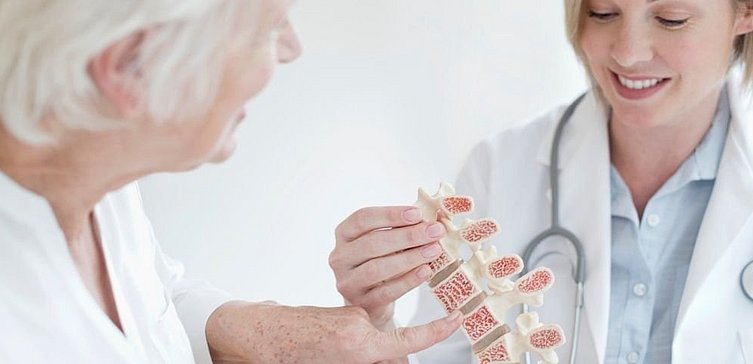 Ältere Frau bekommt von Ärztin Abbildung einer Osteoporose am Knochen gezeigt
