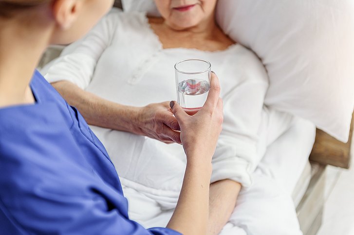 Krankenhausmitarbeiterin gibt Patientin in Krankenbett ein Glas Wasser