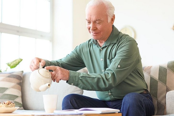 Älterer Mann gießt sich eine Tasse Tee ein