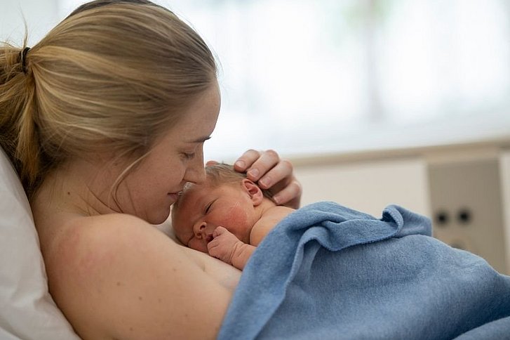 Frau mit Baby im Krankenhausbett beim Bonding