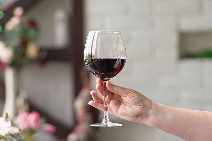 Hand hält ein Glas Rotwein fest