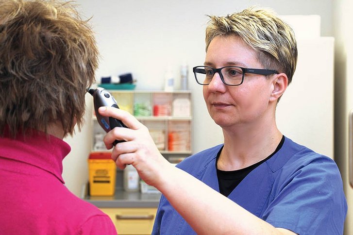 Krankenpflegerin misst Temperatur im Ohr einer älteren Frau